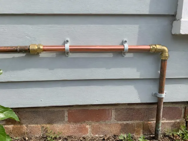 Copper water pipe repair mounted on weatherboard exterior wall above brick base in Lambton