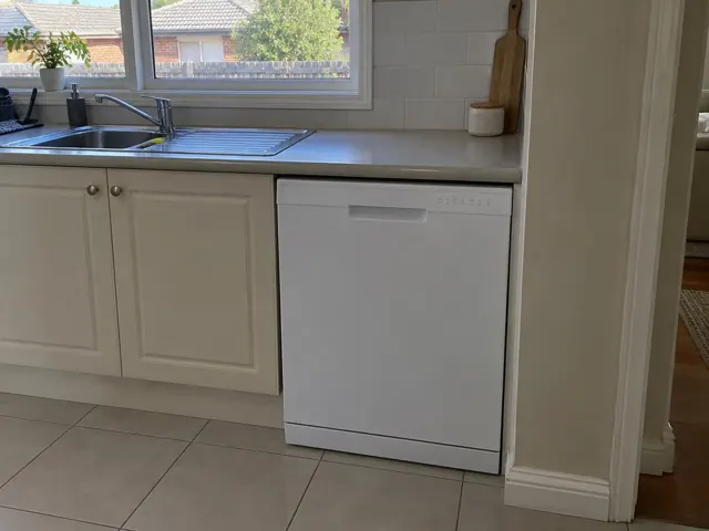 Built-in white dishwasher under a kitchen benchtop beside a sink and tiled floor in Broadmeadow